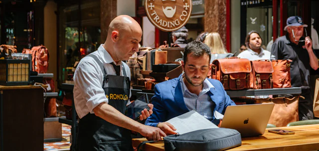 Two people going through paperwork together at the counter of a small leather goods shop